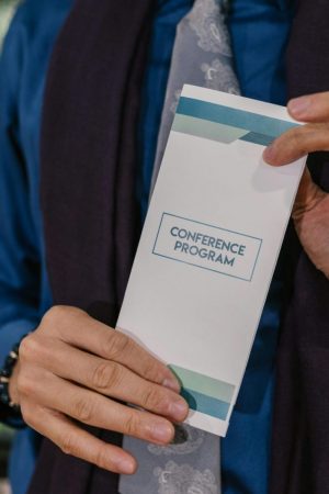Close-up of hands holding a conference program indoors, showcasing formal attire and setting.