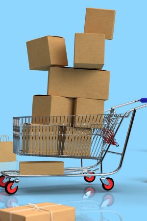 A metal shopping cart with a blue handle is overloaded with brown cardboard boxes of various sizes. More boxes and small shopping bags are scattered on a reflective light blue surface with a solid blue background.